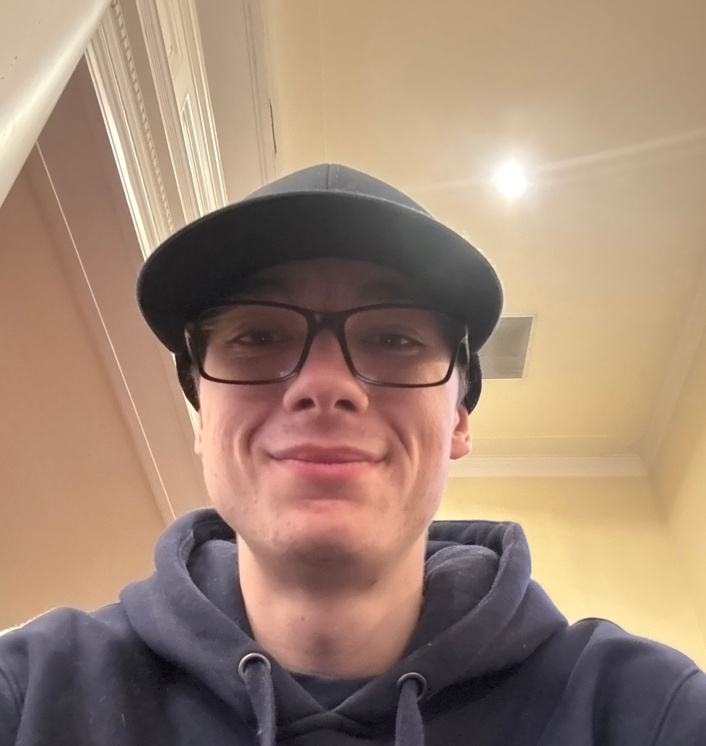 Smiling man wearing glasses and a black baseball cap in a navy blue hoodie.