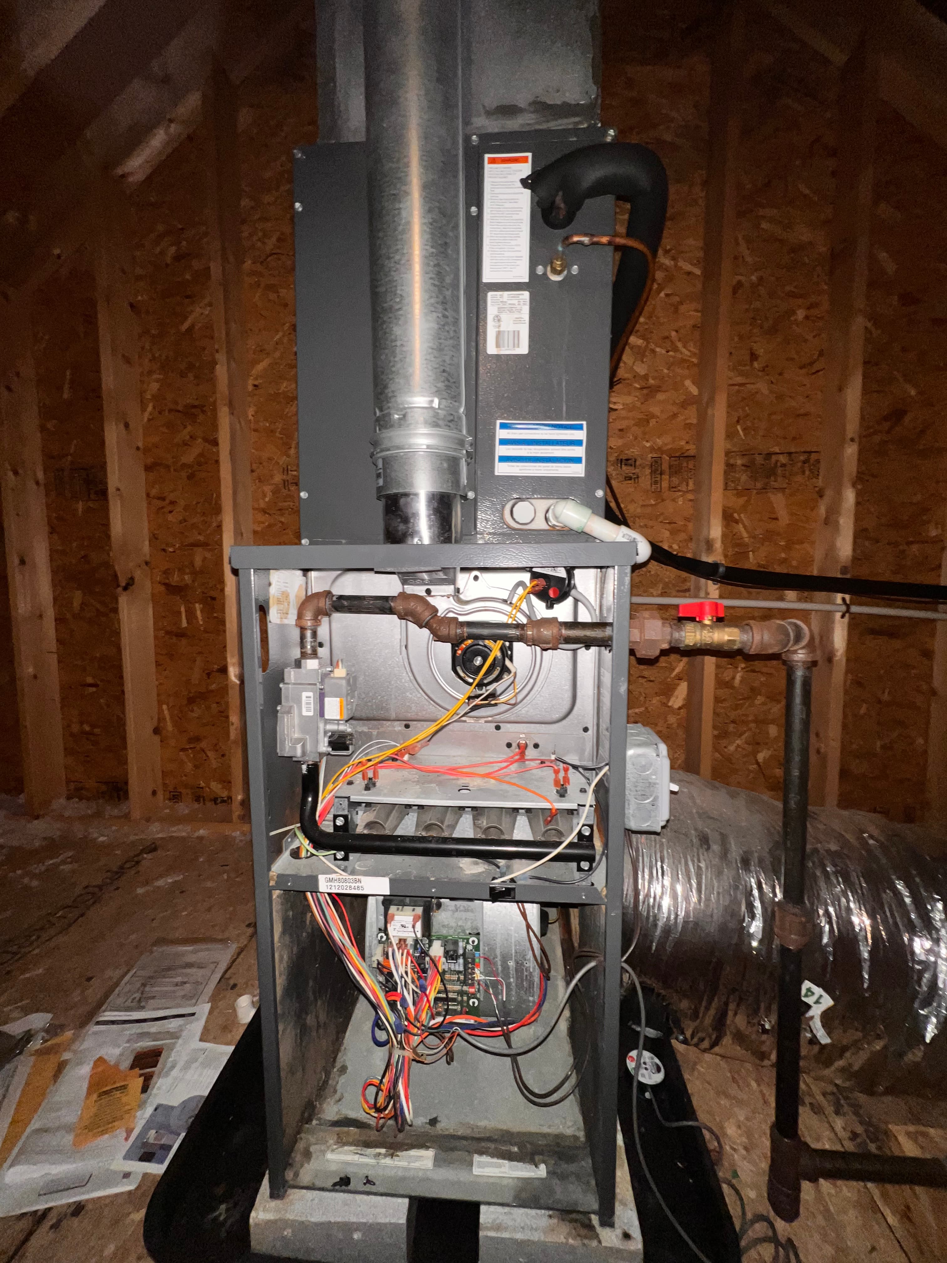Open furnace unit in an attic showing internal wiring, gas lines, and metal ductwork.