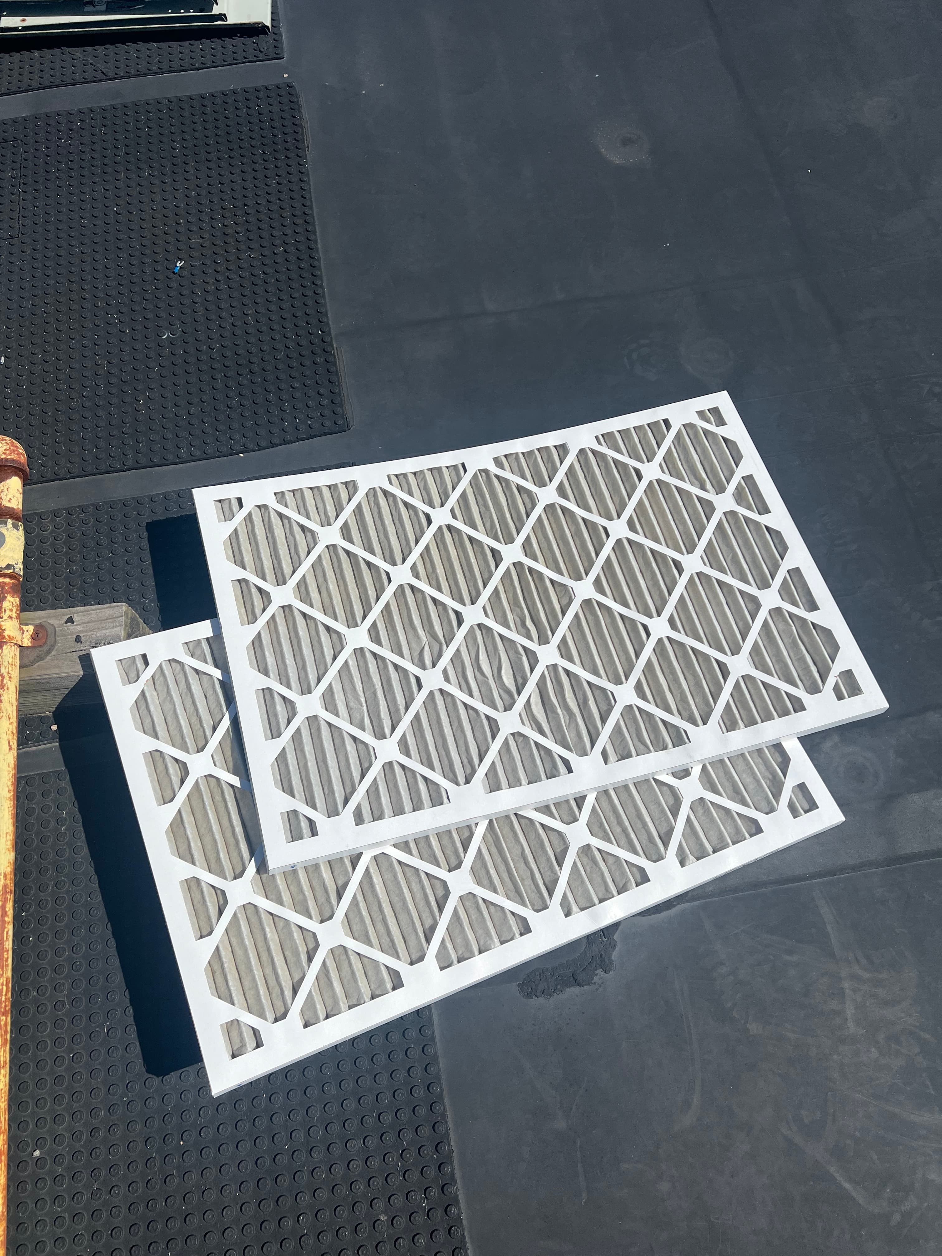 Two white rectangular air filters with diamond-patterned grids resting on a dark, textured flat surface.